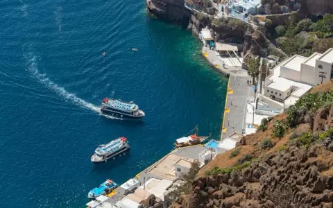 Barche turistiche navigano nel blu intenso del porto di Santorini, con le case bianche aggrappate alla scogliera.