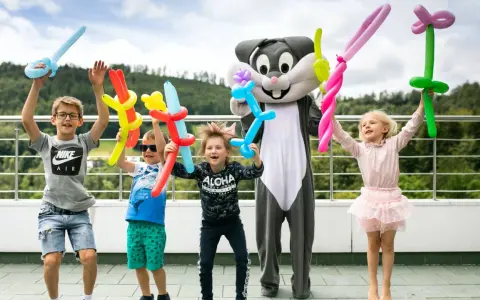 Radosne dzieci z balonami w kształcie zwierzątek i mieczy świętują koniec roku szkolnego z postacią królika.
