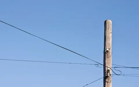 Słup energetyczny z przewodami, symbolizujący zgodę na światłowód nad działką.