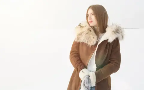 Mujer con abrigo de pelo natural en la nieve, lista para limpiar su ropa de invierno.