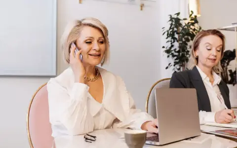Dwie kobiety w biurze, jedna rozmawia przez telefon, druga pisze.