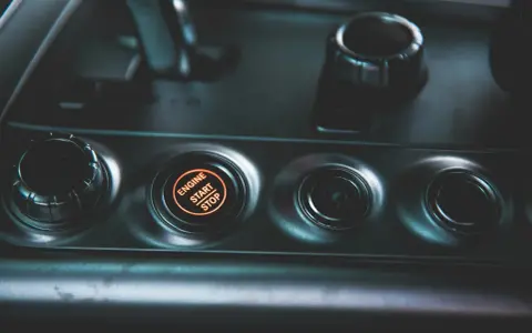 Podświetlany przycisk "ENGINE START STOP" w samochodzie. Obok niego pokrętło wyboru trybu jazdy, jak czujnik IBS.