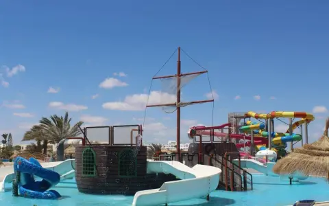 Djerba Aqua Resort (ex. Sun Connect) z pirackim statkiem i kolorowymi zjeżdżalniami wodnymi pod błękitnym niebem.