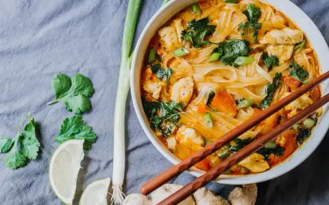 Miseczka z tajską zupą curry z kurczakiem, makaronem ryżowym i warzywami, podana z pałeczkami.