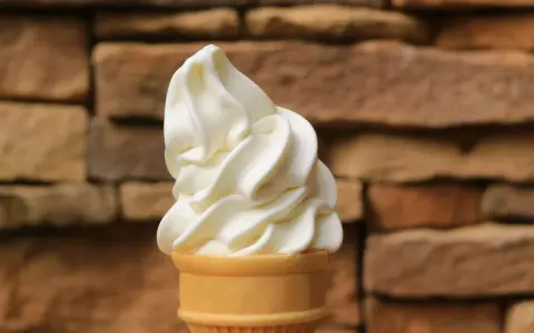 Ein cremiges Vanilleeis mit Ei im Waffelhörnchen, vor einer rustikalen Steinwand.