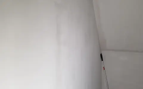 En lång skrapa med handtag står lutad mot en nyspacklad vägg, redo att slipa spackel för en slät yta.