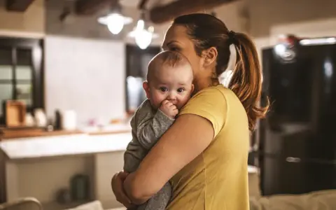 Zmęczona mama tuli dziecko, szukając sposobu, jak oduczyć dziecko jeść w nocy.