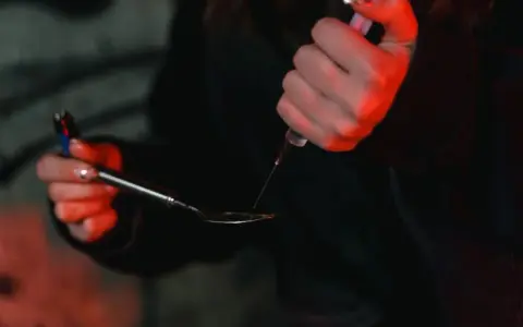 Dłoń trzymająca strzykawkę i łyżkę z płynem, oświetlone czerwonym światłem.