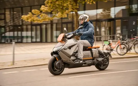 Mężczyzna w kasku jedzie na futurystycznym skuterze BMW CE04 po mieście.