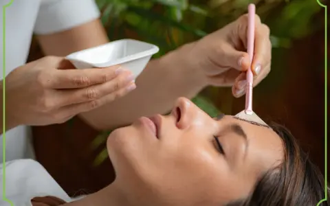 Kosmetyczka aplikuje na czoło klientki peeling z kwasami AHA za pomocą pędzelka.