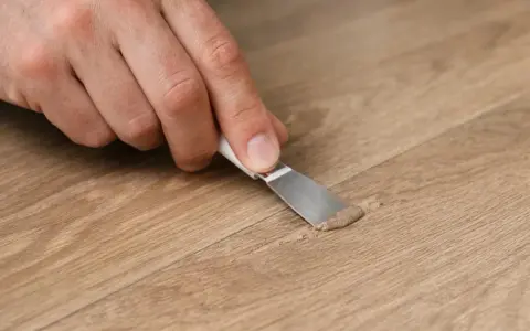 Mano che ripara un piccolo buco nel muro con una spatola e stucco.
