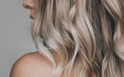 Kobieta z falowanymi, blond włosami ozdobionymi nowoczesnymi pasemkami, ukazana od ramienia.