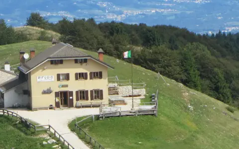 Il rifugio Posa Puner, con la bandiera italiana che sventola, domina un paesaggio montano verdeggiante.