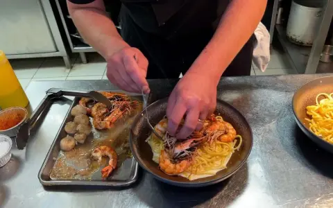 Un chef prépare des pâtes aux crevettes et pétoncles, un plat savoureux de cuisine de terroir.