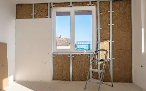 Instalación de un trasdosado de pladur con aislamiento, mostrando la estructura metálica, la lana de roca y una placa de yeso.