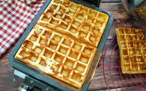 Frisch gebackene belgische Waffeln in einer Waffelform, daneben eine auf einem Rost.
