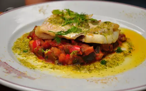 Délicieux dos de cabillaud à la poêle, servi sur un lit de légumes méditerranéens et arrosé d'une sauce verte.