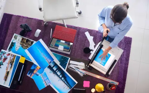 Kobieta przycina wydruki wykonane techniką druk lateksowy. Na stole leżą zdjęcia, laptop i aparat.