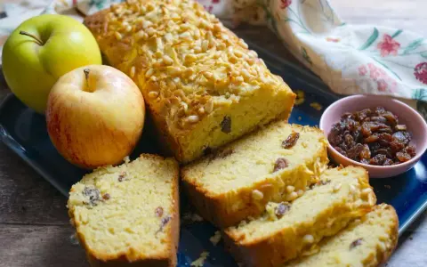 Plumcake alle mele dorato, con pinoli e uvetta, accompagnato da mele fresche e una ciotolina di uvetta.