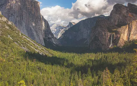 Majestatyczne klify i wodospad w **parku narodowym Yosemite**, otoczone gęstym lasem iglastym.