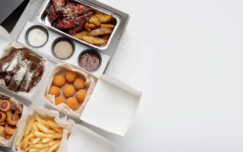 Variedad de comida para llevar: alitas, costillas, papas fritas, croquetas y pan. ¡Todo listo para disfrutar!