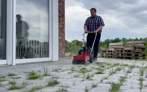 Mężczyzna usuwa chwasty z kostki brukowej za pomocą specjalnej maszyny. To skuteczne domowe sposoby na mech na kostce brukowej.