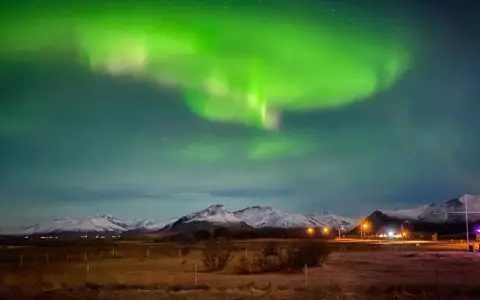 Islandia pogoda luty: zielona zorza polarna nad ośnieżonymi górami i polami.