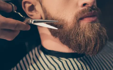 Un barbero recorta una barba larga y rojiza con tijeras.
