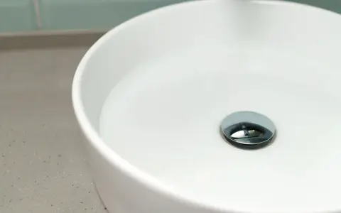 Biała umywalka z chromowanym korkiem klik klak. Dowiedz się, jak wyjąć korek klik klak z umywalki, gdy się zatnie.