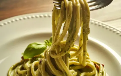 Trenette al pesto, un piatto invitante con pasta fresca avvolta in una salsa verde vibrante, guarnito con basilico.
