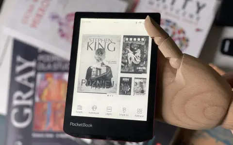 Drewniana dłoń wskazuje na ekran czytnika PocketBook, gdzie wyświetla się okładka książki Stephena Kinga "Później". W tle widać inne książki.
