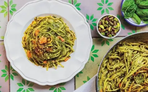 Makaron z pesto ze słoika, posypany pistacjami i kawałkami suszonych pomidorów, prezentuje się apetycznie na talerzu.