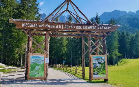 Ingresso in legno per il regno del gigante Baranci, con cartelli informativi e sentiero che si addentra nel bosco.