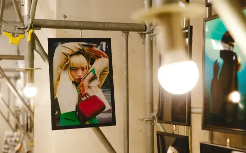 Plakat z kobietą w beżowym płaszczu i zielonym swetrze, trzymającą czerwoną torebkę. Stylizacja przypomina modę z **Pezet Tokyo**.
