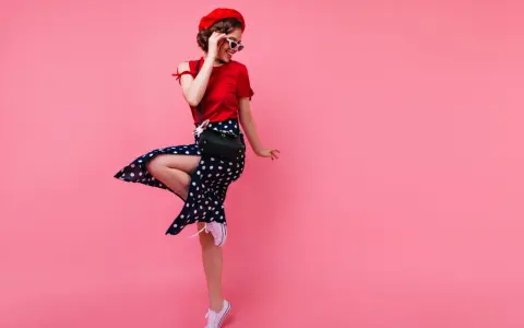 Dziewczyna w czerwonym beretce i sukience w grochy, w stylu pin up, skacze na różowym tle.