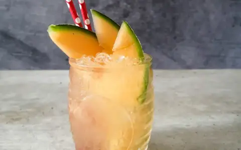 Orzeźwiający drink z mango, ozdobiony plasterkami owocu i dwoma czerwono-białymi słomkami. Idealny na upalne dni.