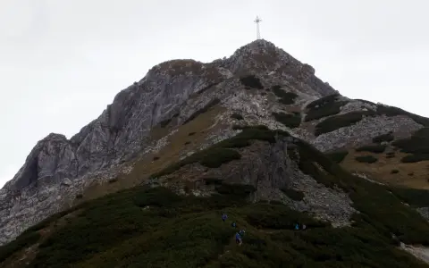 Grupa turystów podąża szlakiem na Giewont. W oddali widać charakterystyczny krzyż na szczycie.