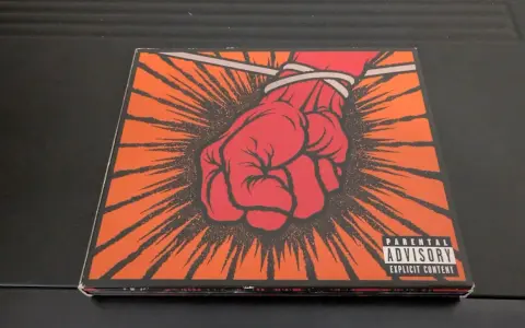 Okładka płyty Metallica "St. Anger" z czerwoną, zawiązaną pięścią i napisem "Parental Advisory".