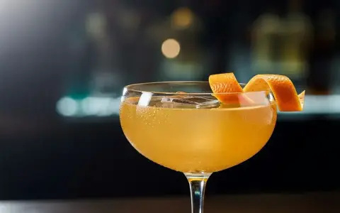 En gyllene cocktail i ett coupeglas, garnerad med en apelsinzest. Ett klassiskt, old fashioned recept som lockar.