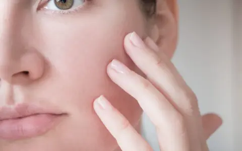 Dita accarezzano delicatamente il viso, mostrando una pelle reattiva e sensibile, bisognosa di cure delicate.
