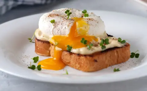 Un delicioso huevo poche con yema líquida cayendo sobre tostadas, adornado con brotes verdes y pimienta.
