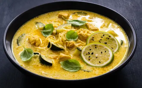 Aksamitne curry z kurczakiem, makaronem i plasterkami cukinii, ozdobione świeżą bazylią i limonką.