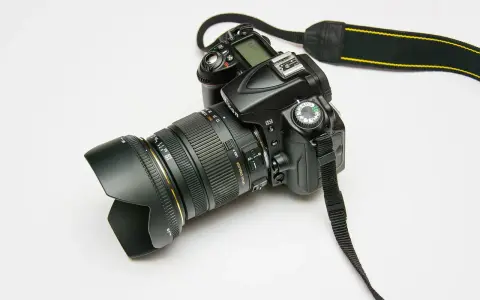 Czarny aparat fotograficzny z obiektywem i paskiem na białym tle.