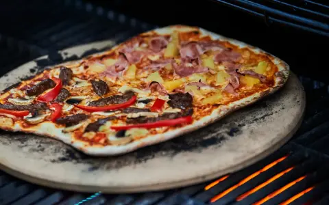 En läcker pizza på grillen med skinka, ananas, kött och paprika. En perfekt sommarmåltid!