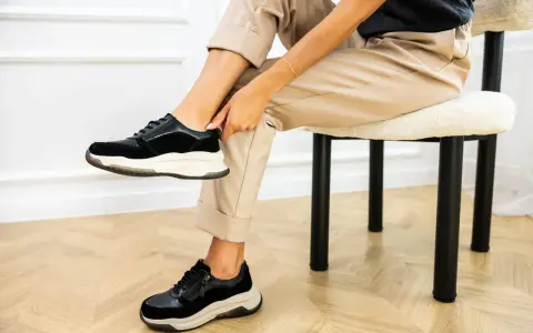 Kobieta w beżowych spodniach i czarnych sneakersach na grubych podeszwach. Pokazuje, jak szybko wysuszyć buty, by znów cieszyć się komfortem.