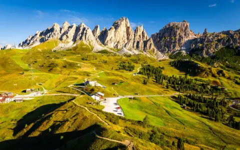 Panorami mozzafiato sull'**Alta Via numero 2 Dolomiti**. Sentieri serpeggianti tra prati verdi e imponenti vette rocciose sotto un cielo azzurro.