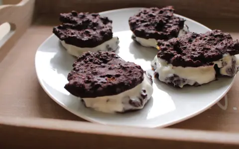 Cztery domowe ciastka z kremem, przypominające Oreo, na białym talerzu. Pyszna przekąska, choć warto sprawdzić oreo kcal przed zjedzeniem.