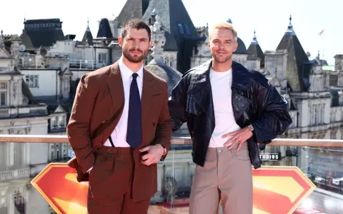 Due uomini posano con stile: uno in completo marrone, dimostrando come abbinare il marrone uomo con eleganza, l'altro con giacca di pelle e pantaloni chiari.