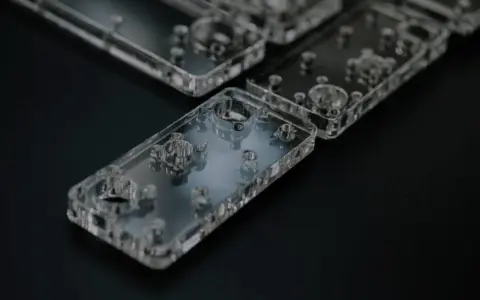 Rows of clear acrylic phone cases, showcasing their intricate internal designs and precise cuts, are laid out on a dark surface.