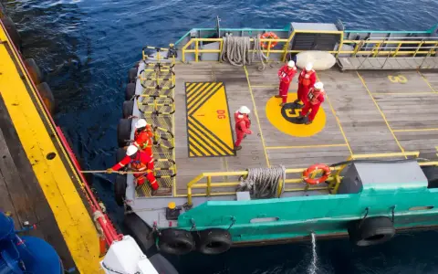 Équipage en combinaison rouge ajustant la longueur du bout de remorquage du bateau. Ils travaillent sur le pont d'un navire, manœuvrant une corde.